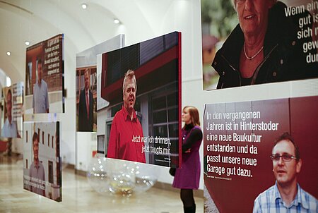 Photo of a room in which large-format photographs of people hang.
