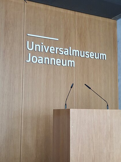 The lectern in the Auditorium at Joanneumsviertel stands on the stage platform with the lettering Universalmuseum Joanneum on the back wall.