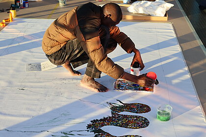 Famakan Magassa in der Needle als die Sonne untergeht, dementsprechend goldig sind die Lichtspiegelungen über der Acrylarbeit 