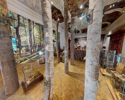 Screenshot from a 360 degree tour. You can see the exhibition room "Of forest and wood" with tree trunks in the middle of the room.