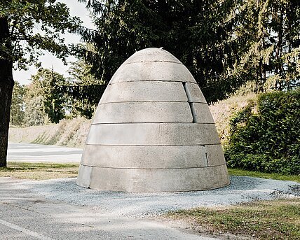 A concrete bunker in the shape of a beehive or warhead with three vertical openings. These resemble embrasures. There is a metal hatch at the top.