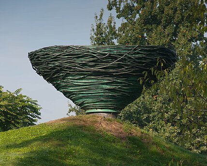 Kienzer's sculpture made of coiled copper tubing rises above the hilltop like a giant bird's nest. The object thus looks like a mirror image or inverted continuation of the hill. The material also refers to the eternal cycle of change in nature, in that it changes itself through oxidation and becomes part of nature.