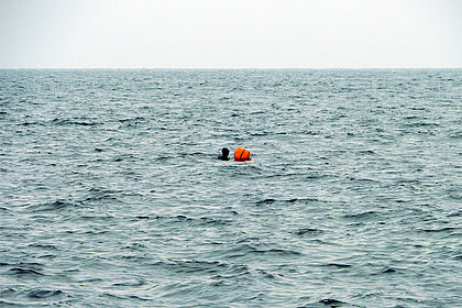 Blick auf das offene Meer mit einer Person in einem Neoprenazug neben einer orangefarbenen Boje