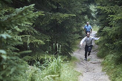 Ein Künstler der Compagnie La Fabrique Royale läuft einen schmalen Waldweg bergab.