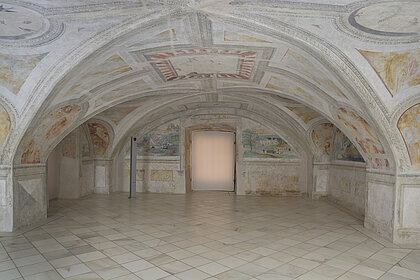 Photograph of a room with a vaulted ceiling. Frescoes in bright colours are painted on the ceiling.