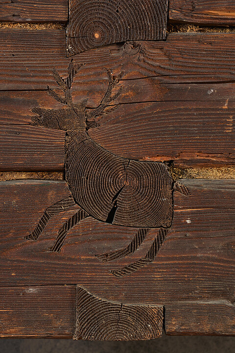 In eine Holzwand ist in die Stämme ein weiterer Stamm in Form eines Hirsches eingelassen.