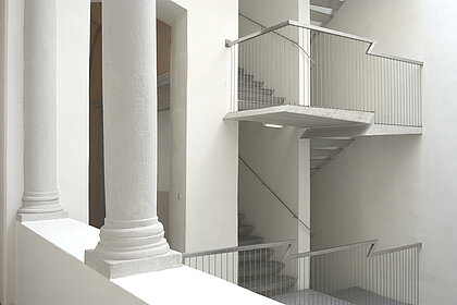 White staircase with metal banister. Two columns in the foreground