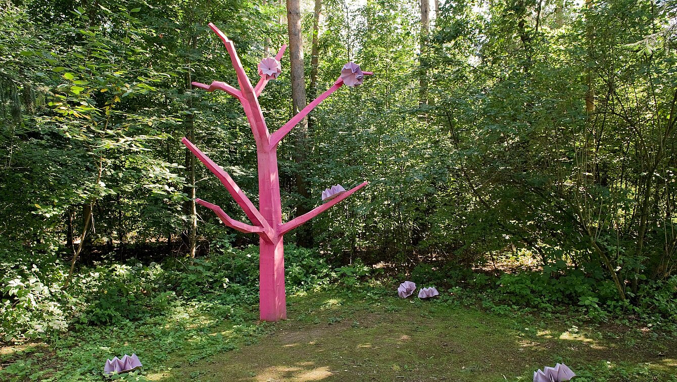 Die Skulptur Asoziale Tochter steht als abstrahierte und reduzierte Baumform zwischen Mischwaldbäumen und innerhalb des Unterholzes und Gebüsches einer Lichtung.