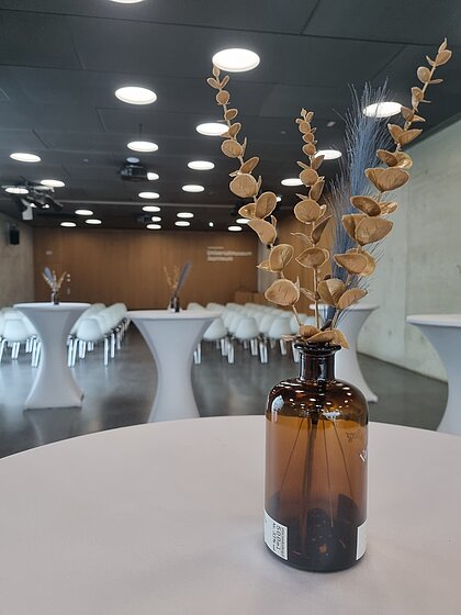 Im Auditorium im Joanneumsviertel sind im Hintergrund Richtung Bühne Sessel aufgebaut. Im Vordergrund stehen Stehtische mit Dekoration.