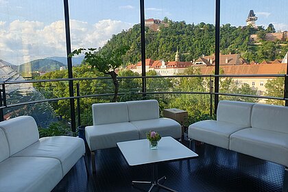 View of the Schlossberg from the Needle in the Kunsthaus Graz. In the foreground are white couches and a small table.