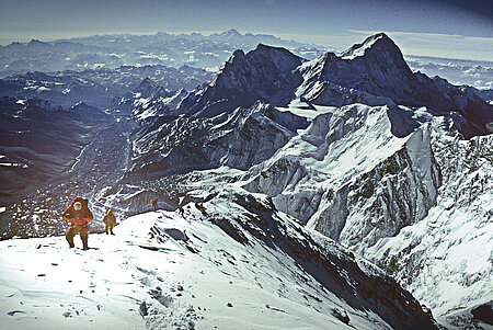 A man walks over a snowy mountain ridge.