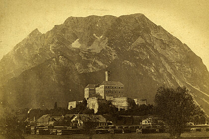 Old photograph of Trautenfels Castle. The castle stands in front of the Grimming mountain. The photo is coloured yellow.