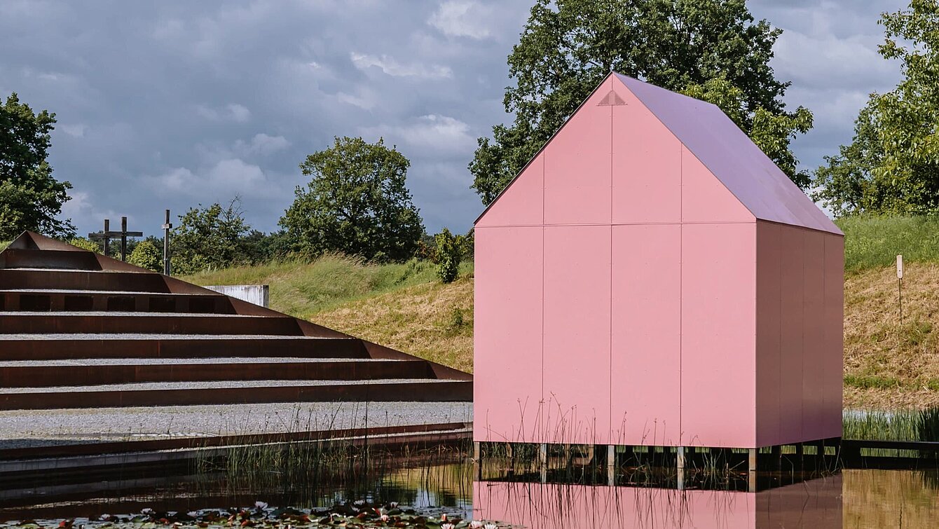 Am Seerosenteich neben dem Berggartencafé steht ein kleines rosa Einfamilienhaus. Über einen Steg zugänglich können drei Projektionen im Inneren begutachtet werden. 
