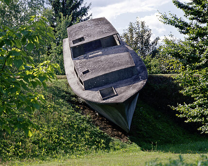 Eine Betonskulptur in der Form eines realen Bootes scheint auf der Hügellandschaft des Skulpturenparks zu schwimmen. 