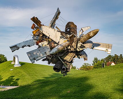 Blick vom Wegesrand auf die Skulptur "Airplane Parts & Hills" von Nancy Rubins und "Die Erdkugel als Koffer" von Peter Weibel in der Ferne