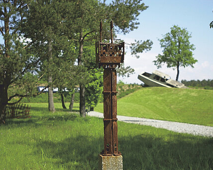 Gerhard Moswitzer's metal sculpture stands on a patch of grass in the Alpine Garden. In the background you can see other sculptures in a blur. 