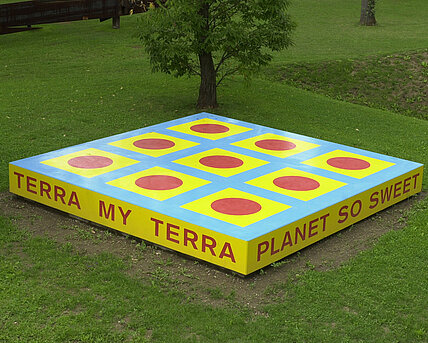 The sculpture is a platform with the inscription "TERRA MY TERRA/PLANET SO SWEET/I CAN FEEL YOU/UNDER MY FEET". [inscriptions translated from german]