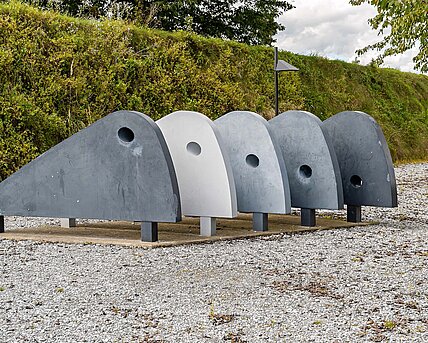 The "walking machine" by Karin Hazelwander consists of five winged elements in different shades of gray. It looks as if it could start moving at any time. The hole in each element shifts from the upper edge of the first curve to the lower edge of the fifth and last, suggesting an imaginary movement.